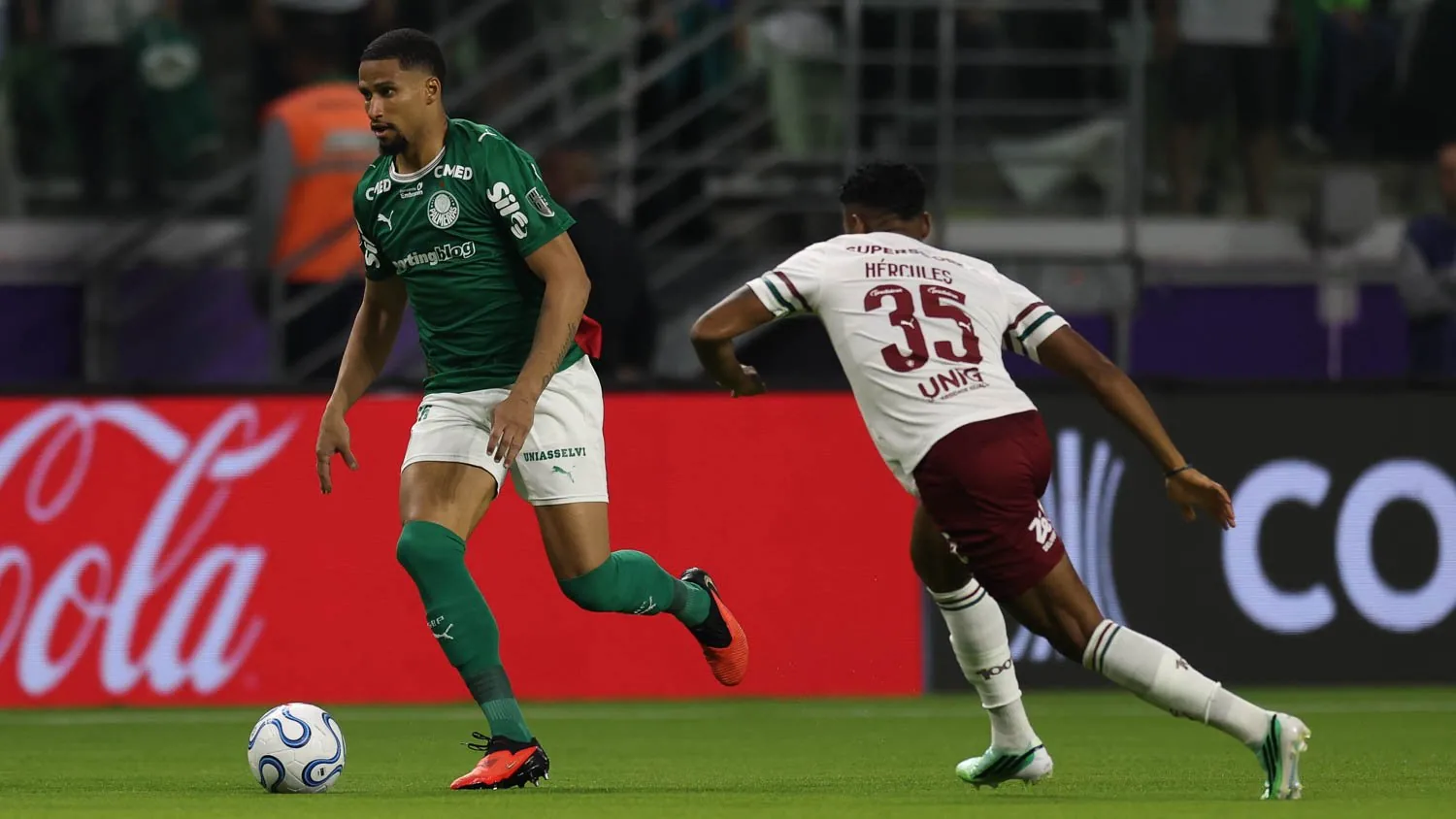 Murilo conduz a bola pelo Palmeiras, acompanhado por Hércules, do Fluminense, no gramado do Nubank Parque.