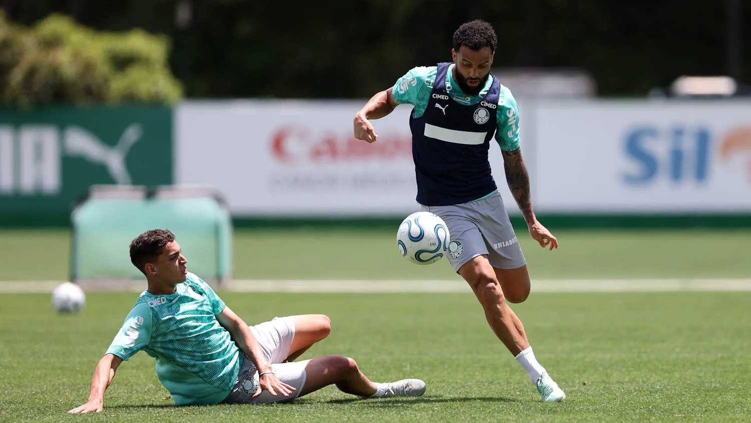 Jogador do Palmeiras conduz a bola em treino na Academia de Futebol, enquanto outro atleta tenta o desarme de carrinho.